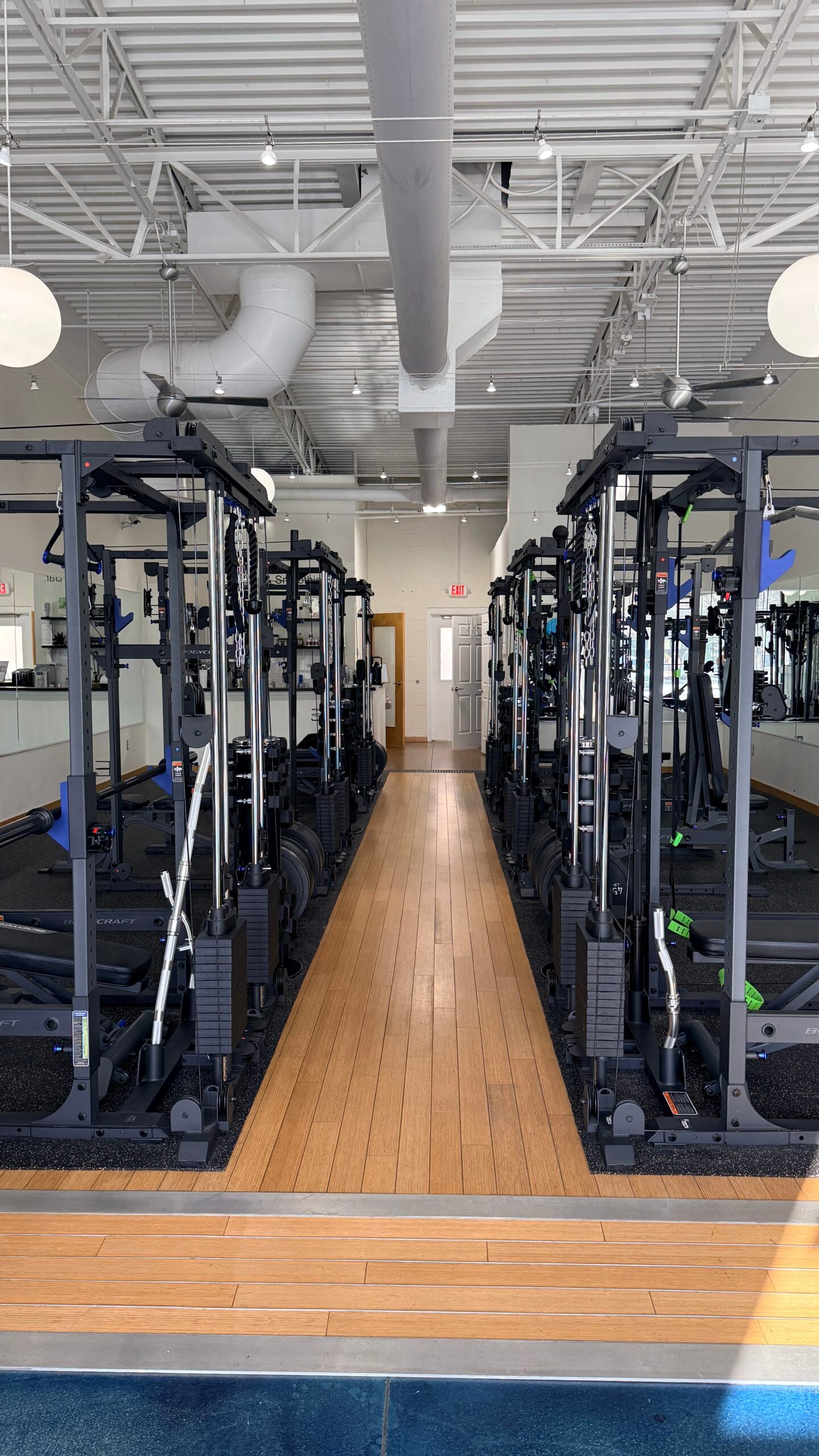 Row of dual cable machines lining a wood-floor aisle in a modern Asheville personal training studio.