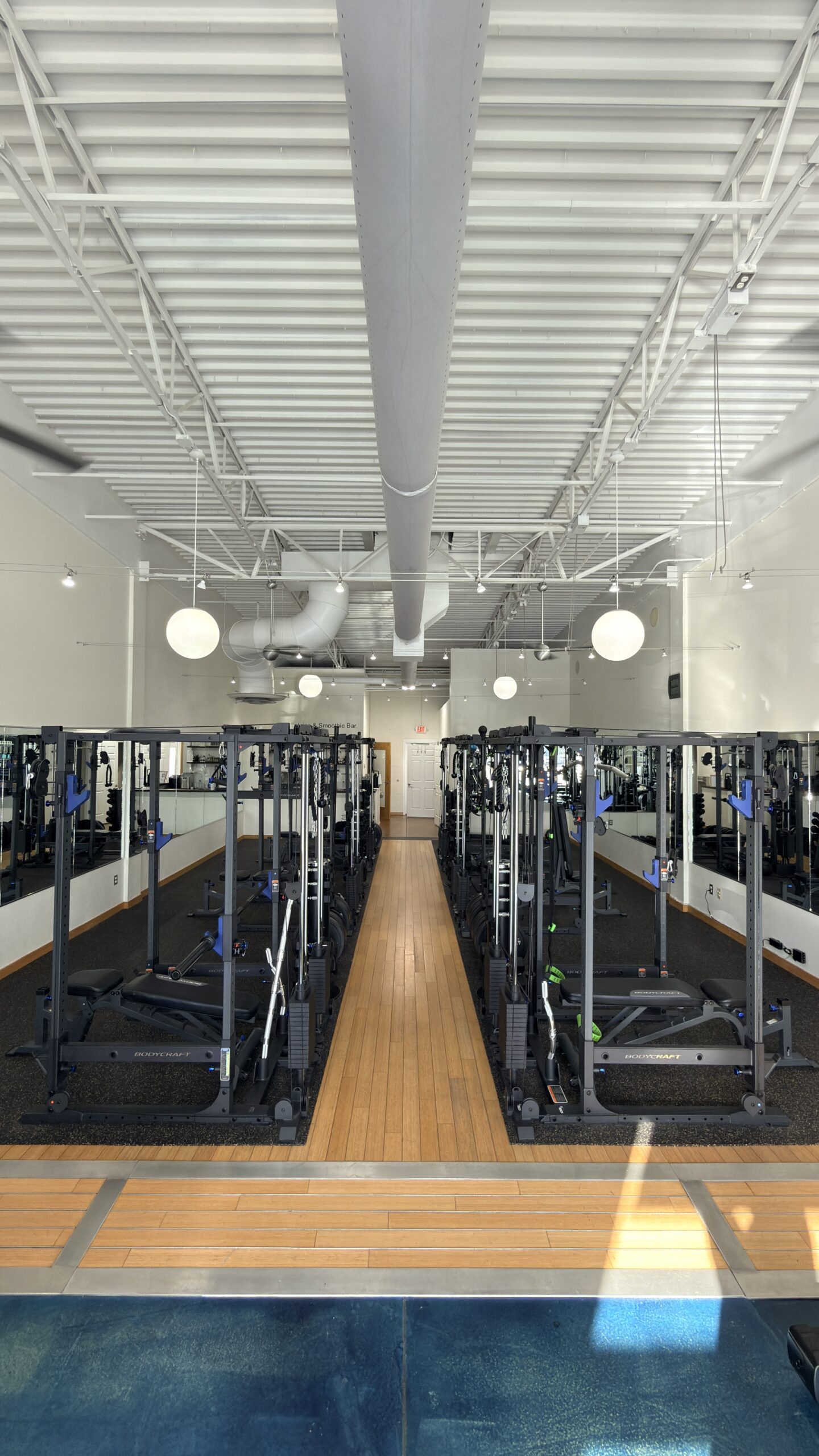 Two rows of BodyCraft cable machines line a wood-floored personal training studio with mirrored walls.