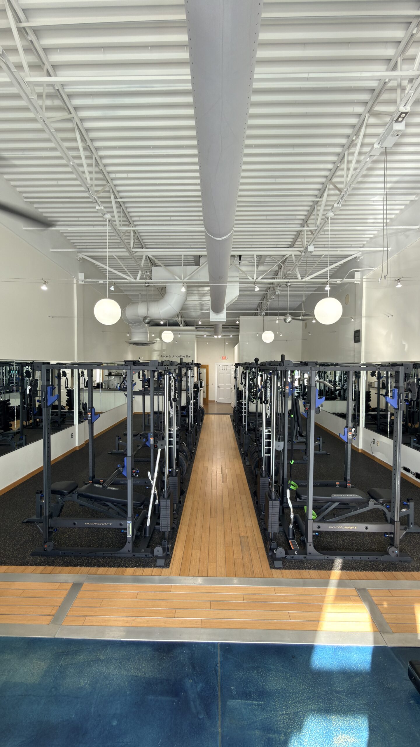Rows of BodyCraft cable machines fill a spacious, well-lit Asheville gym with hardwood floors.
