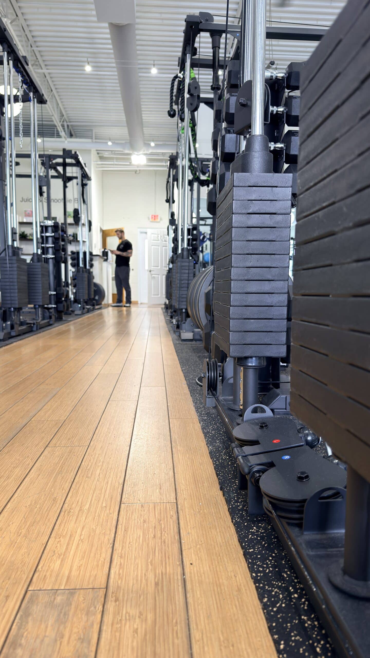 Row of cable machines on hardwood floor in a bright Asheville personal training studio with trainer in background.