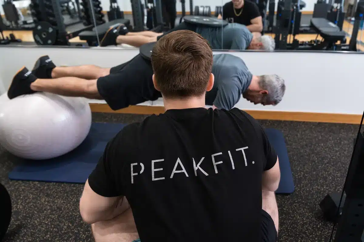 Personal trainer guides older client through stability ball exercise on gym floor