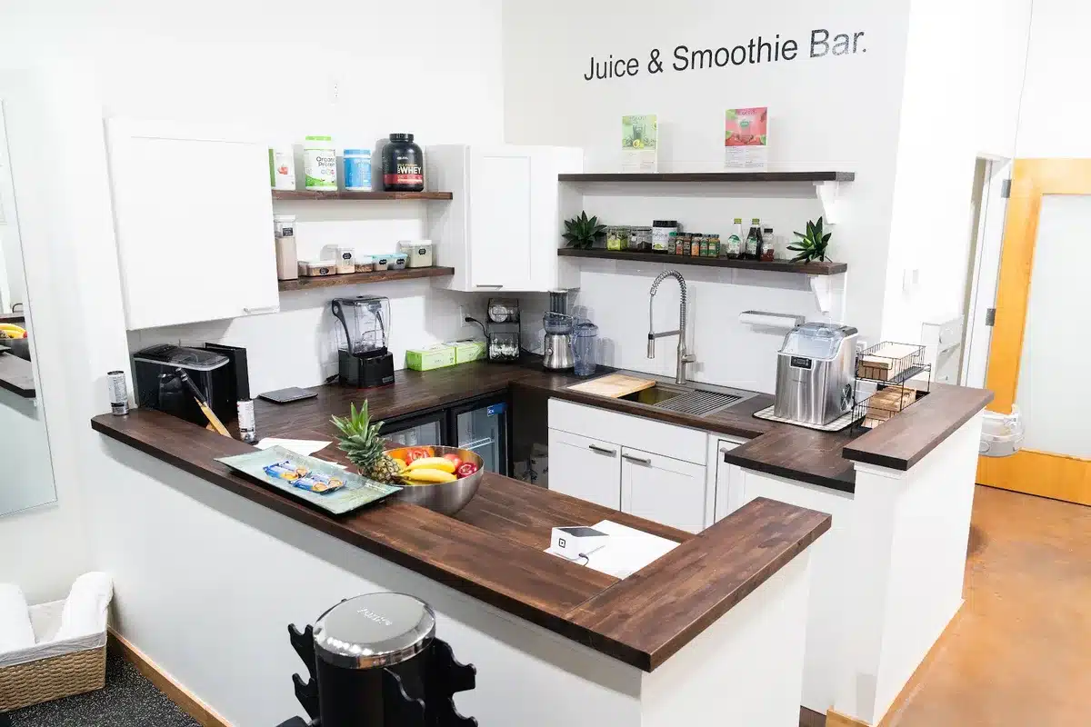 Juice and smoothie bar with dark wood counters, blenders, fresh fruit, and supplement shelves