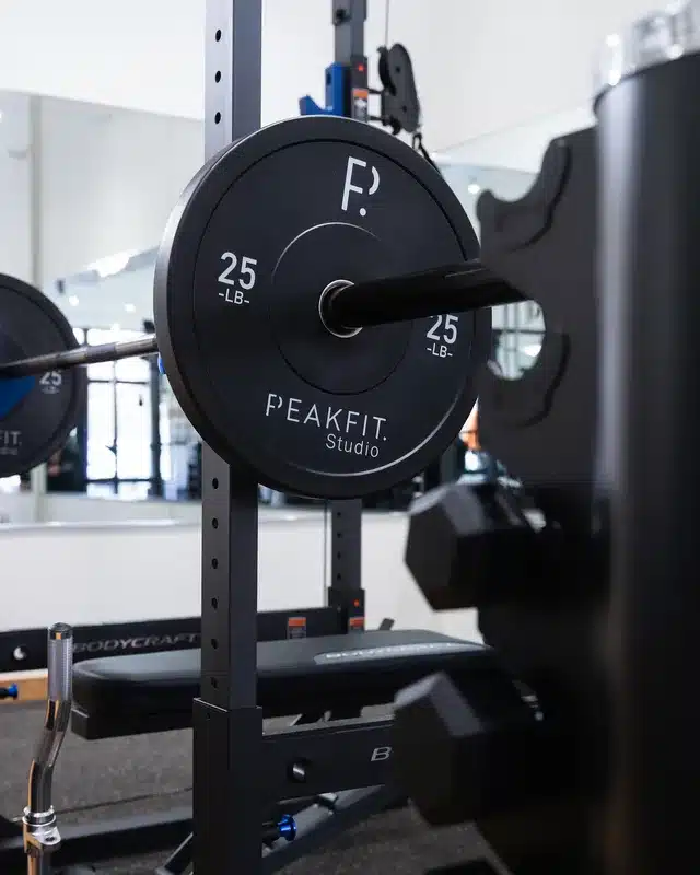 25-lb bumper plates loaded on barbell in squat rack at PeakFit Studio gym