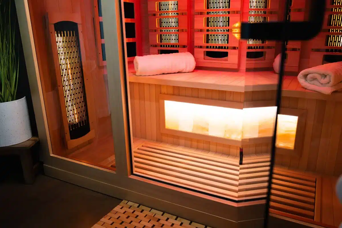 Infrared sauna cabin with red heating panels glowing cedar wood benches rolled white towels and Himalayan salt wall