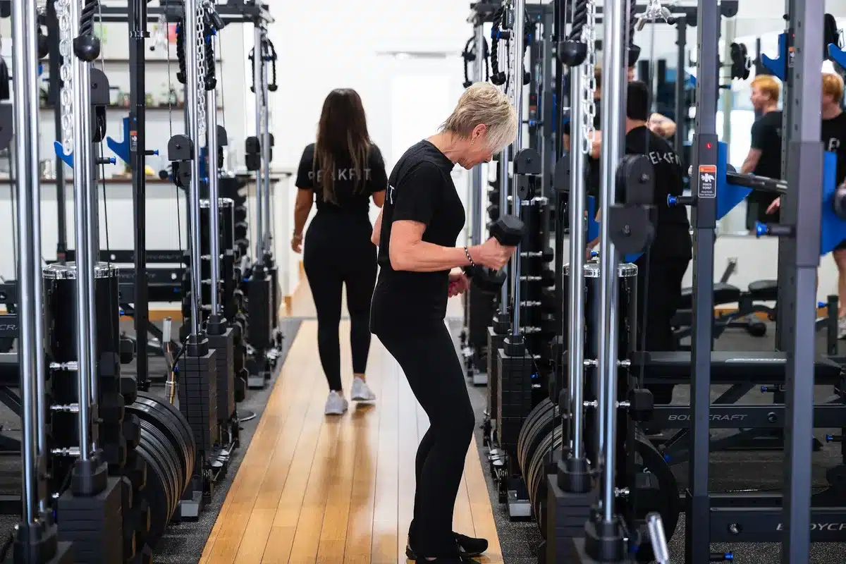 Two women in black workout clothes training with dumbbells and cable machines in a modern gym