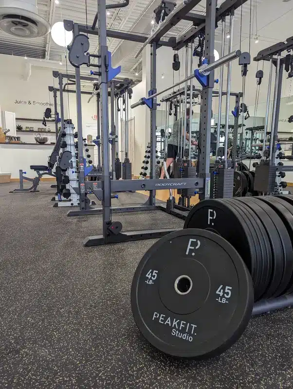 45-lb bumper plates on floor rack beside Bodycraft cable machines in bright gym